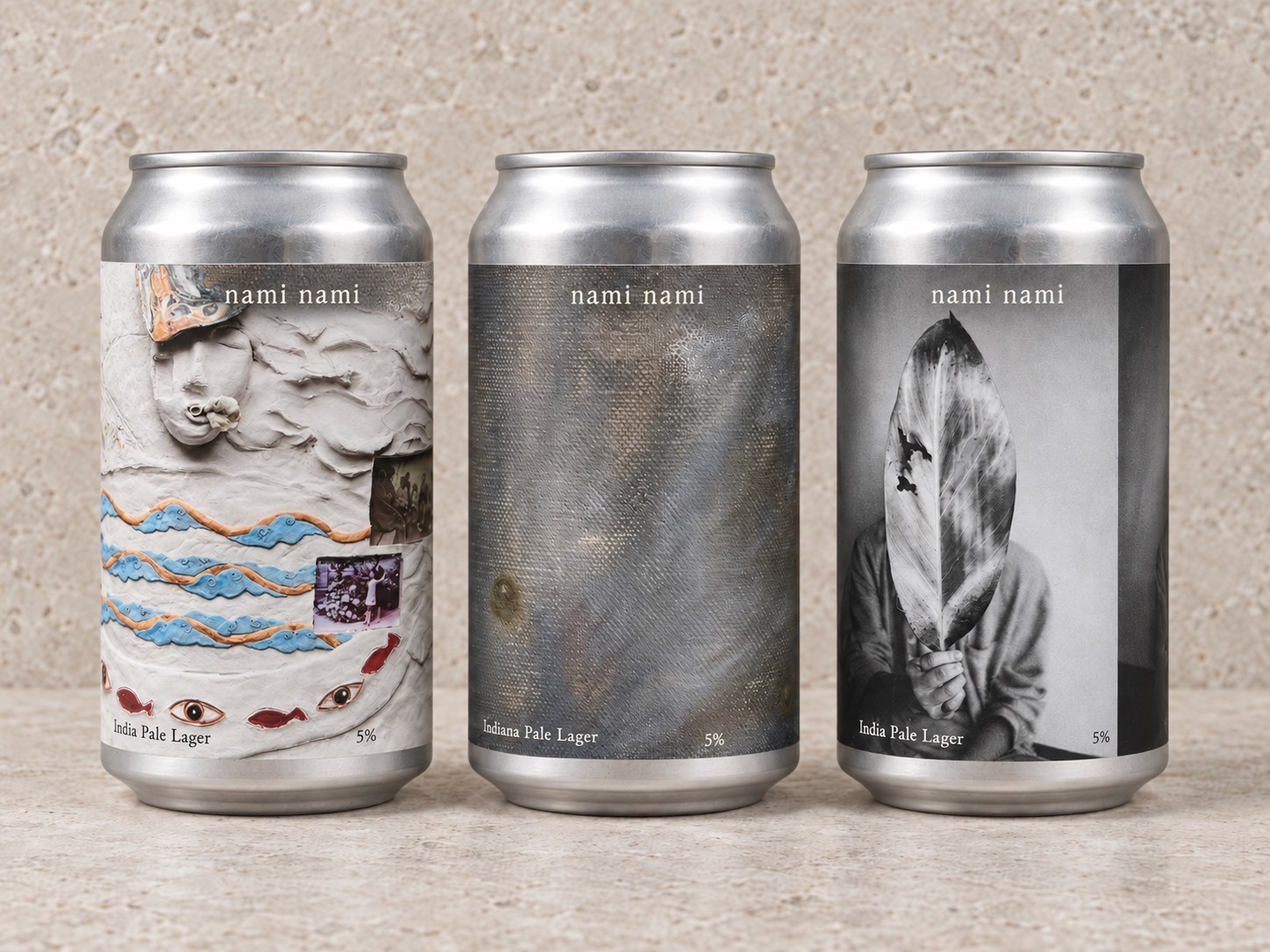 Three nami nami cans, each wrapped in a different artist’s work: a clay relief with waves and fish, a muted oil painting on canvas, and a black-and-white photograph of a figure holding a leaf over their face.